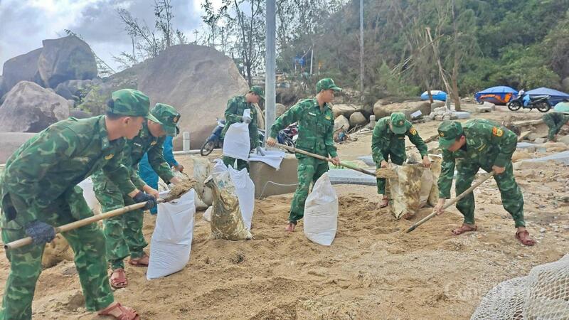 Các chiến sĩ lấy cát để chèn chống nhà cửa giúp dân.